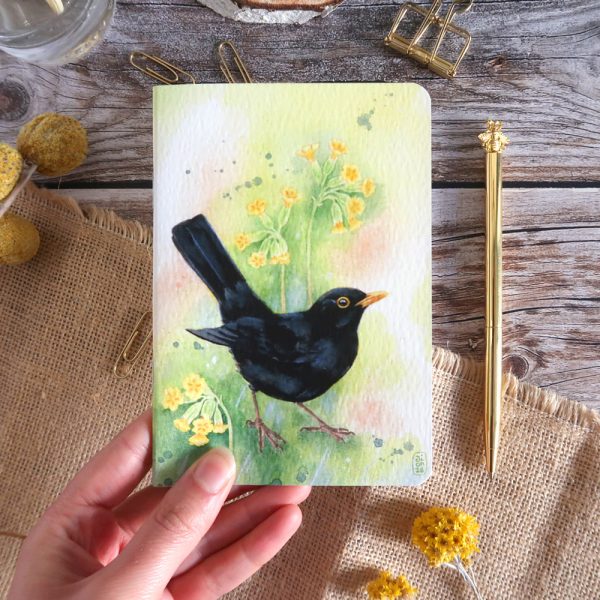 carnet de notes illustré à l'aquarelle d'un merle noir avec des primevères